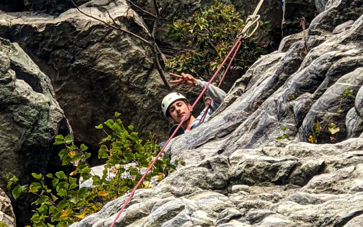 a student gives a peace sign while rock climbing